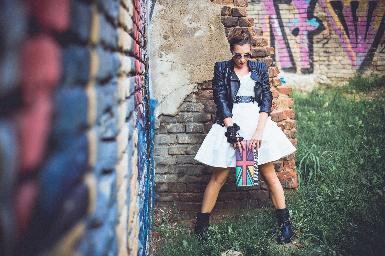 Ona u beloj haljini i kožnoj jakni uz grafitni zid sa Union Jack torbom
