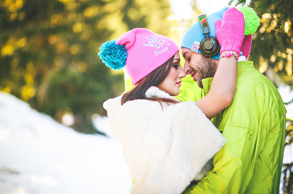 Par u neon odeci pozira na snegu pored fluo zelenog zida od cveća