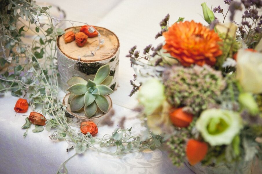 Dekoracija stola — sukulente na drvenim balvančićima sa narandžastim cvećem