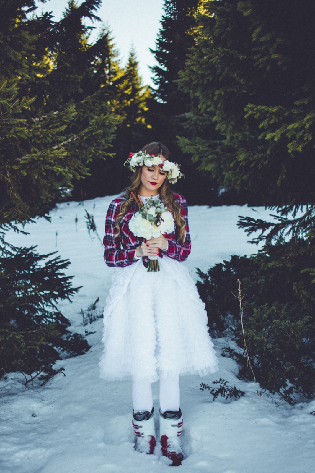 Mlada Nena u kariranoj košulji i cvetnom vencu, stoji u snežnoj šumi sa buketom