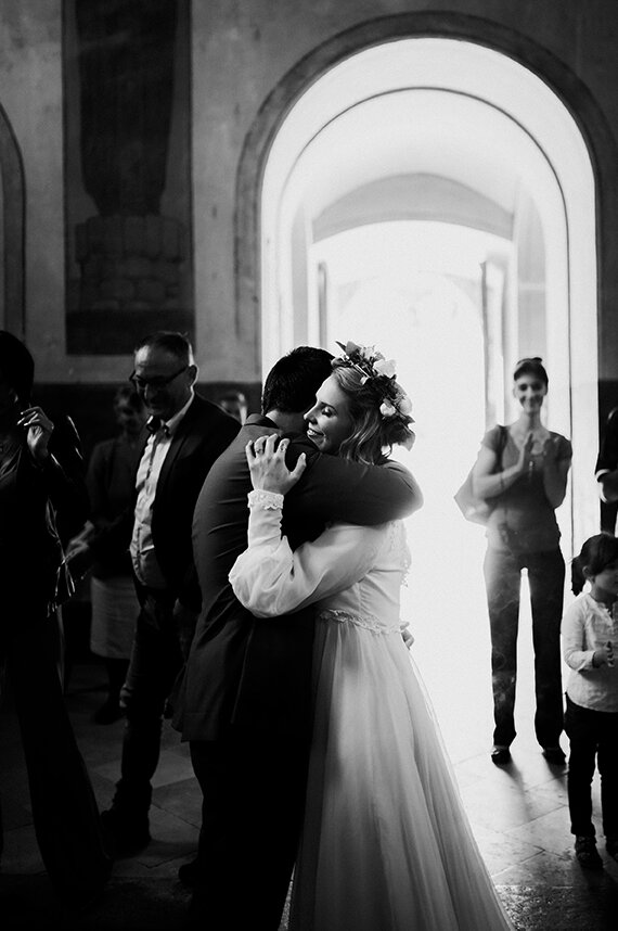 Par se grli u crkvi — crno-bela fotografija, svetlost prolazi kroz luk