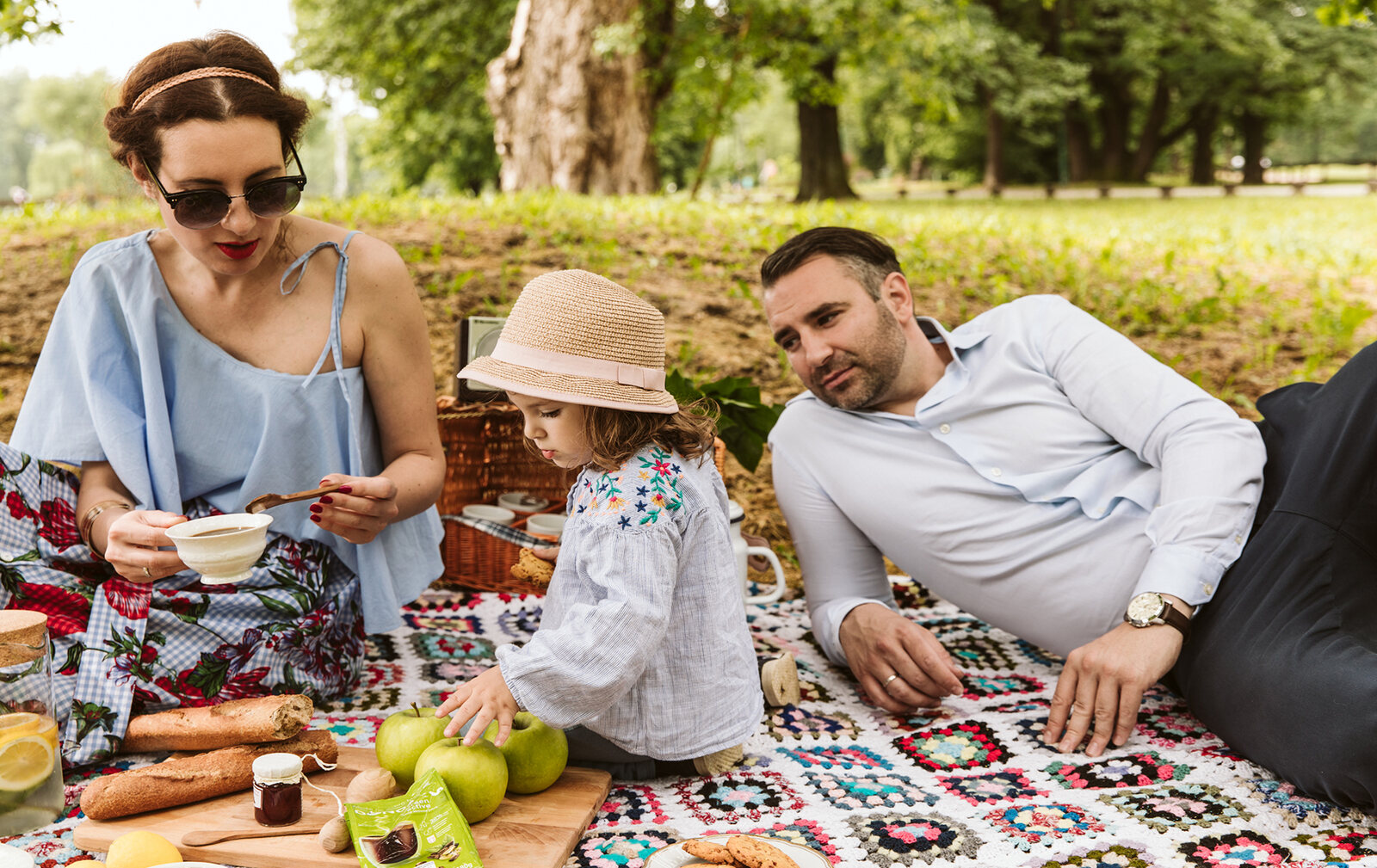 Porodica na pikniku u parku, leži na ćebetu sa piknik korpom
