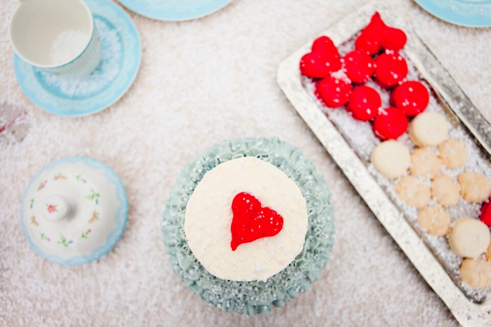 Pogled odozgo na tortu sa crvenim srcem, makaronse i porcelanski set na snežnoj podlozi